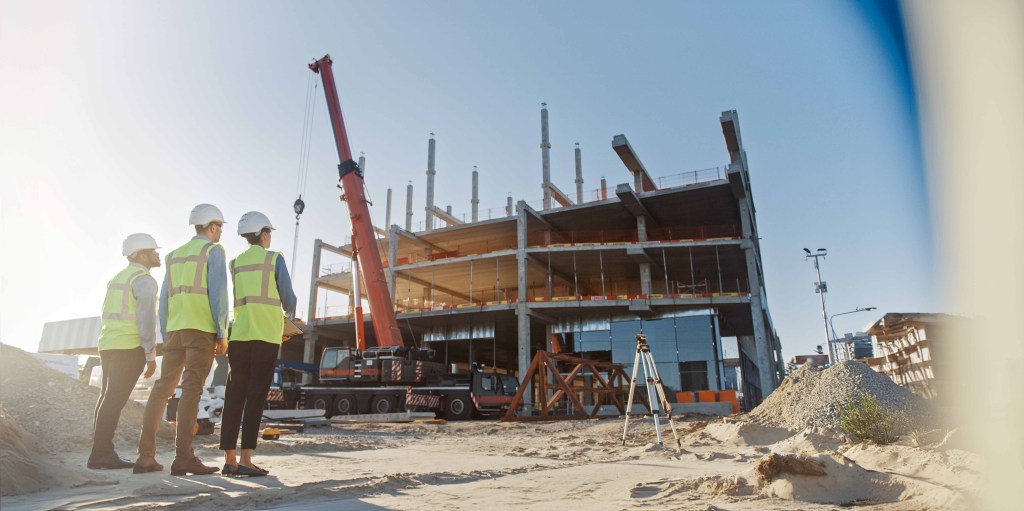 Diverse Team of Specialists Inspect Commercial, Industrial Building Construction Site. In the Background Skyscraper Formwork Frames